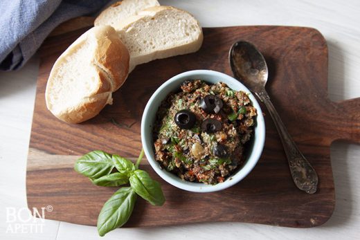 Tapenade met zongedroogde tomaten in een kom op een plankje met brood